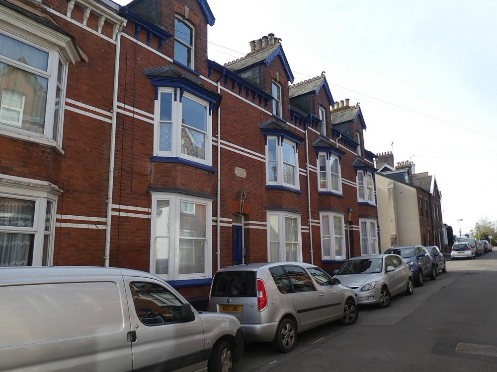 Victorian terraced houses in Exeter with two-storey bay windows, decorative brick banding, and steep slate roofs